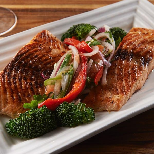 Two grilled salmon fillets with broccoli and a fresh vegetable salsa on a white rectangular plate.