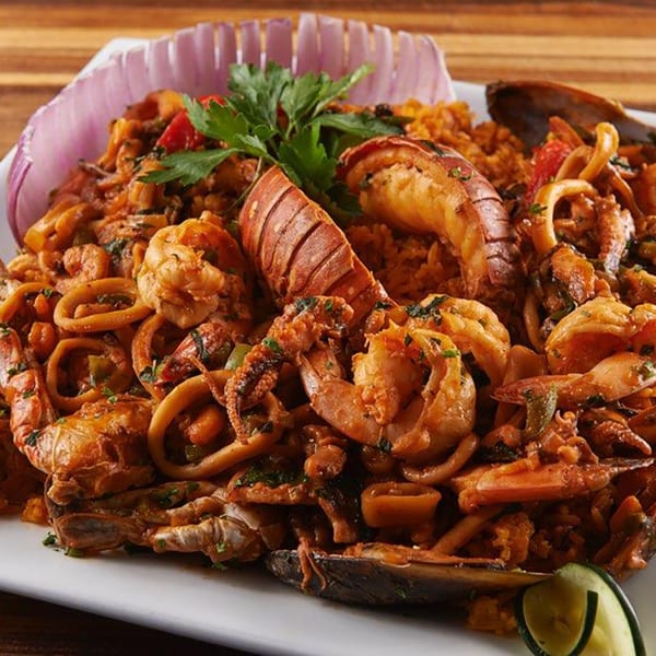 A large platter of seafood paella with lobster, shrimp, mussels, and calamari, garnished with parsley and red onion.