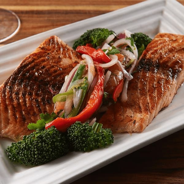 Two grilled salmon fillets with broccoli and a fresh vegetable salsa on a white rectangular plate.