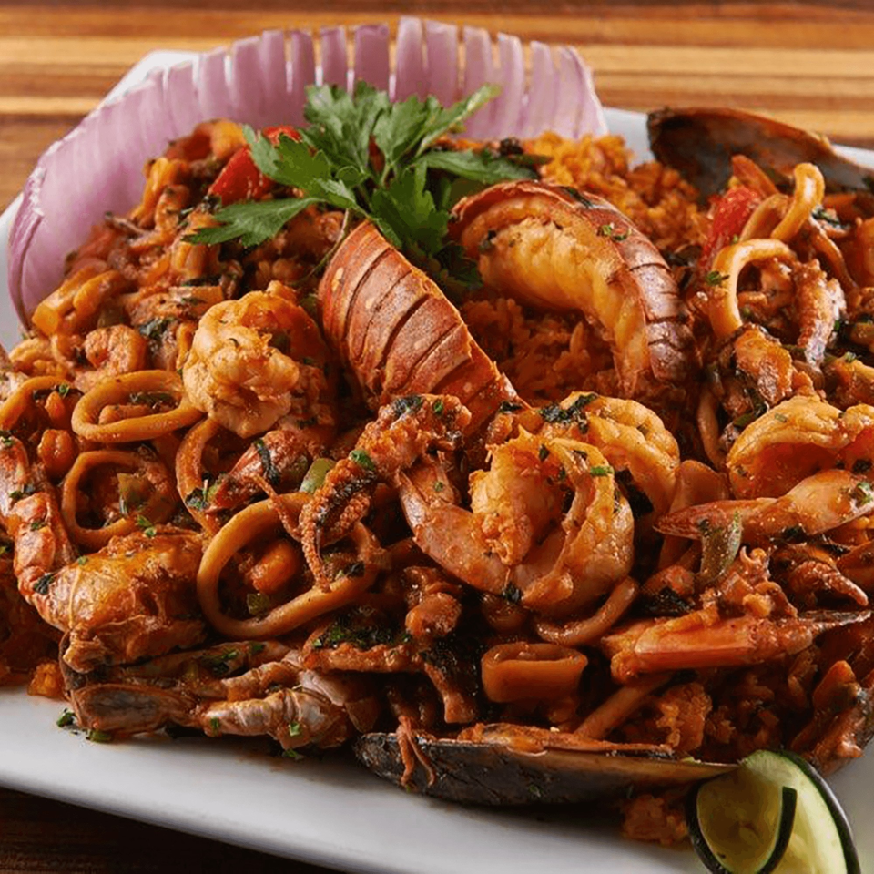 A vibrant seafood paella with lobster, shrimp, mussels, and calamari, garnished with parsley and red onion.