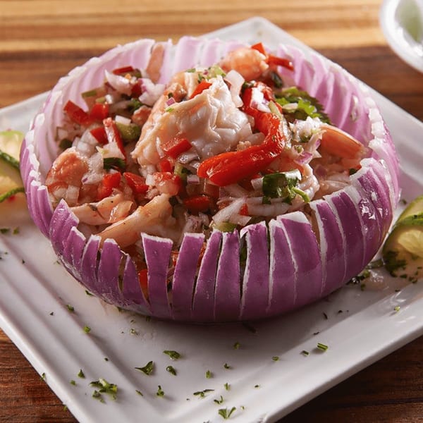 Shrimp ceviche with red peppers and onions, served in a carved red onion bowl on a white plate.