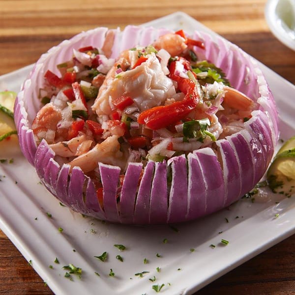 Shrimp ceviche with red peppers and onions, served in a carved red onion bowl on a white plate.