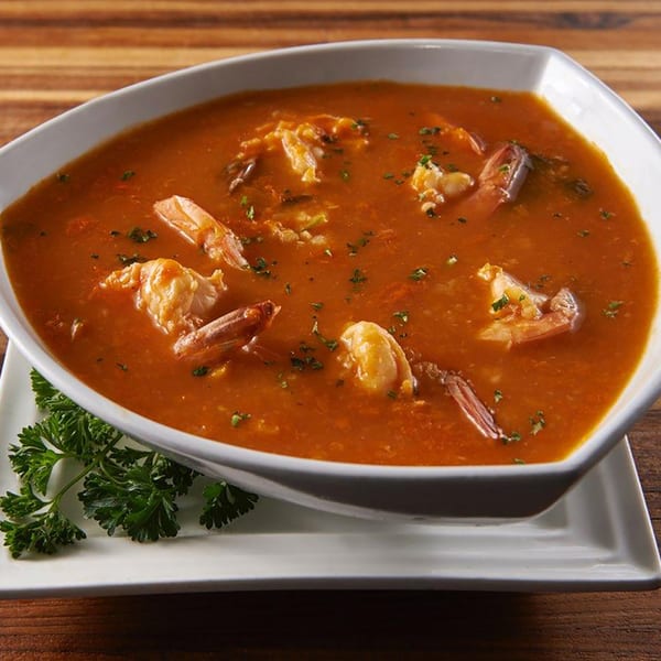 A white bowl of rich orange-red shrimp bisque, garnished with parsley, on a wooden table.