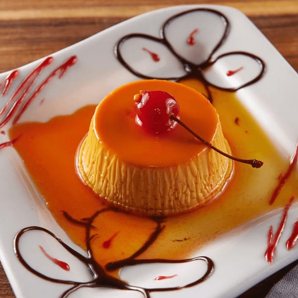 Flan dessert with caramel sauce and a cherry on top, garnished with chocolate and raspberry drizzles.