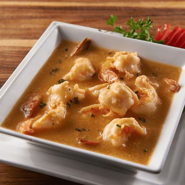 Shrimp in a rich brown sauce, garnished with parsley and red pepper, served in a white bowl.