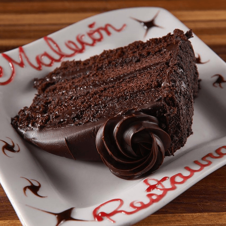A slice of chocolate cake with chocolate frosting and a chocolate swirl on a white plate.